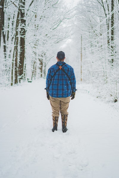 白天，穿着蓝红色夹克和棕色裤子的男子在积雪覆盖的地面上行走